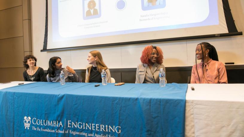 Five female students sit on the student panel, smiling and answering questions. 